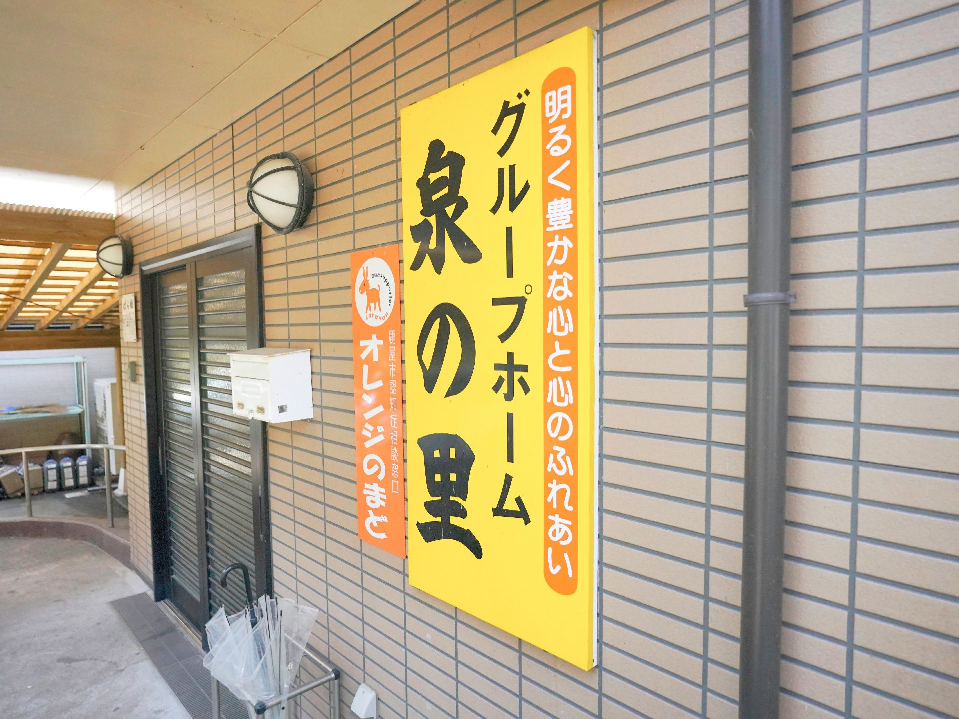 薬を飲もうとしている高齢女性のそばにはエプロンを付けた女性スタッフがいてコップを持っている。