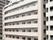 柔らかい色合いが印象的な大型のマンションタイプの建物。一階の入り口付近のスペースには植物が植えられている。