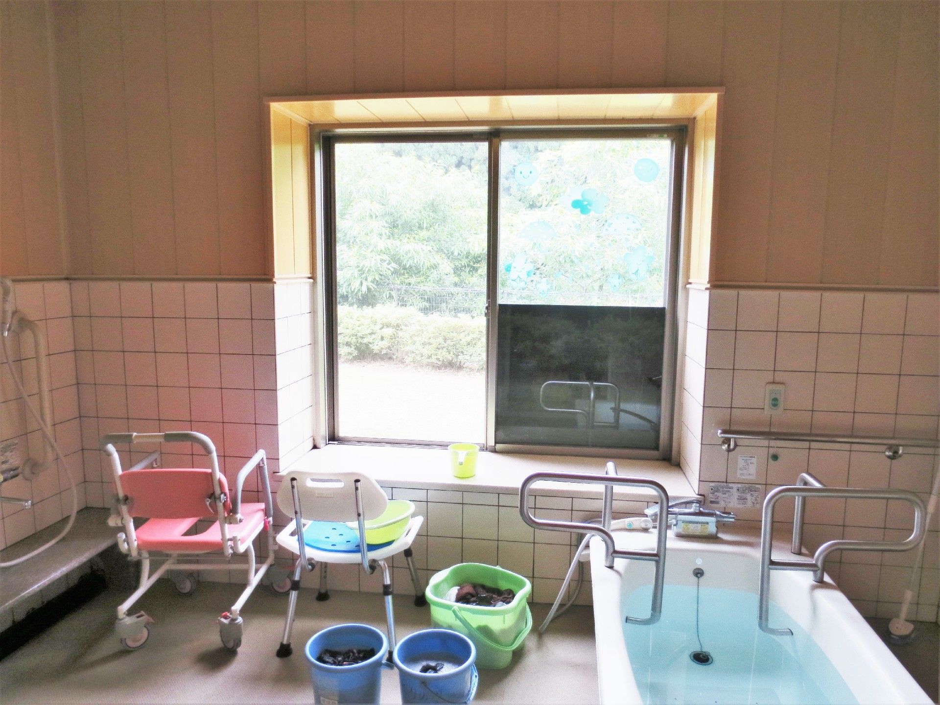 大きな窓が付いた浴室はとても明るく、一人用の浴槽やシャワーチェア、洗い物が入ったバケツなどがある。