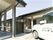 駐車場に施設名付きの車が止まっている様子。平屋建ての大きめの建物が写っている写真