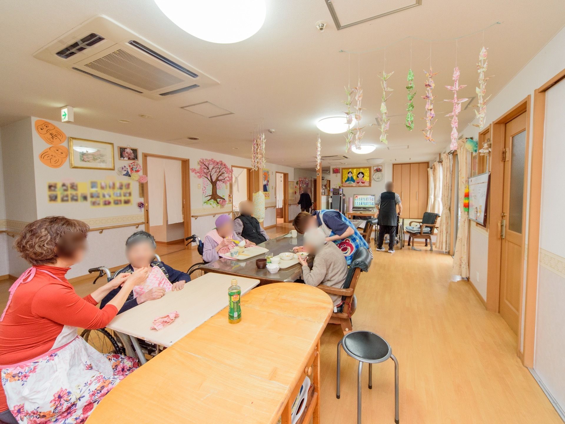 テーブルセットが並べられた、広いフロアがある。入居者が席について、スタッフと一緒に食事をとっている。