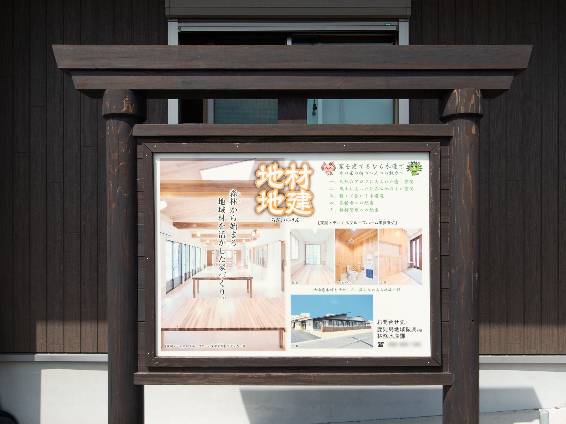 看板が建物の前に立てられ、木造建ての住まいの魅力が複数の写真入りで紹介されている。後ろの窓の上部に、シャッターが取りつけられている。