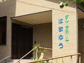 ホーム名がブルーとグリーンの文字で書かれたベージュの外壁の建物は日当たりのいい場所に建っている。