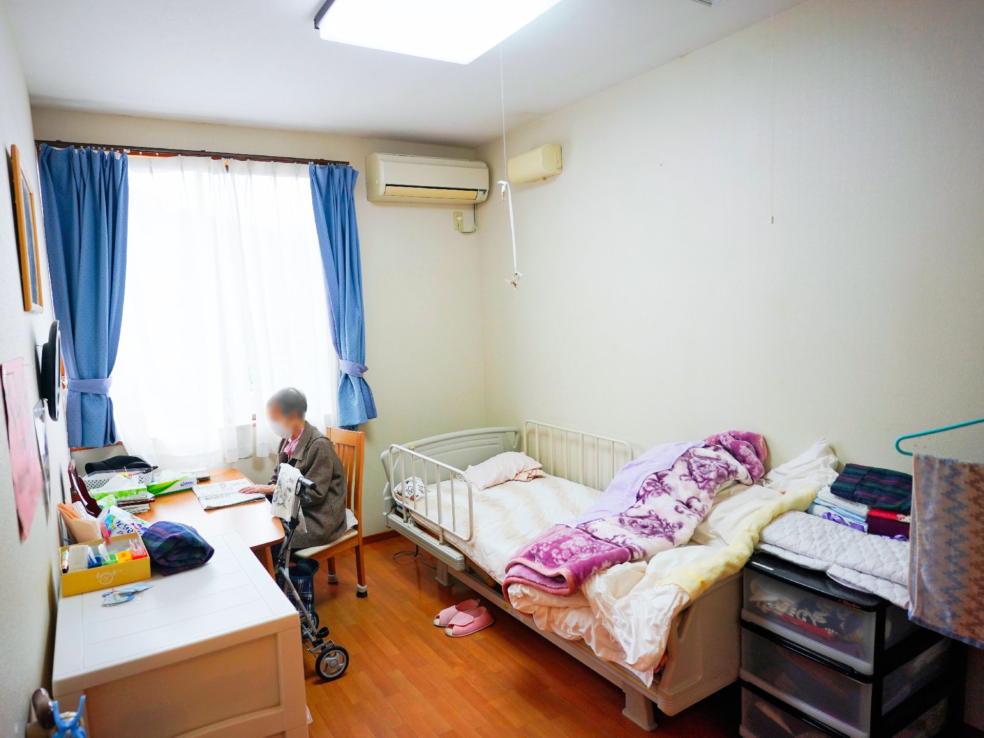 窓があり、介護ベッド、テーブル、椅子が設置されている居室