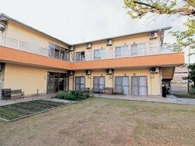 オレンジの屋根が付いた２階建ての建物は2階にベランダがあり、敷地内には野菜畑や庭もある。