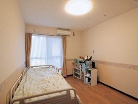 フローリングの部屋には大きな窓が付いている。寝具付きのベッドや収納ケースが置かれている。