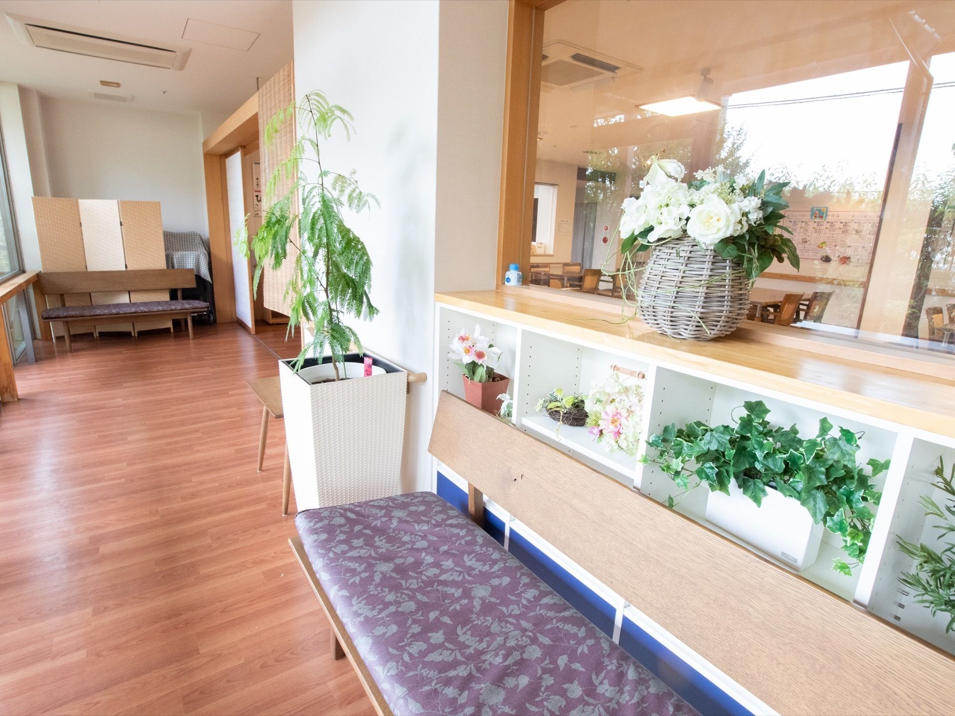 壁に沿って長椅子が置かれている。壁は棚になっており、観葉植物や、かごに入った花が飾られている。天井にエアコンが埋め込まれている。