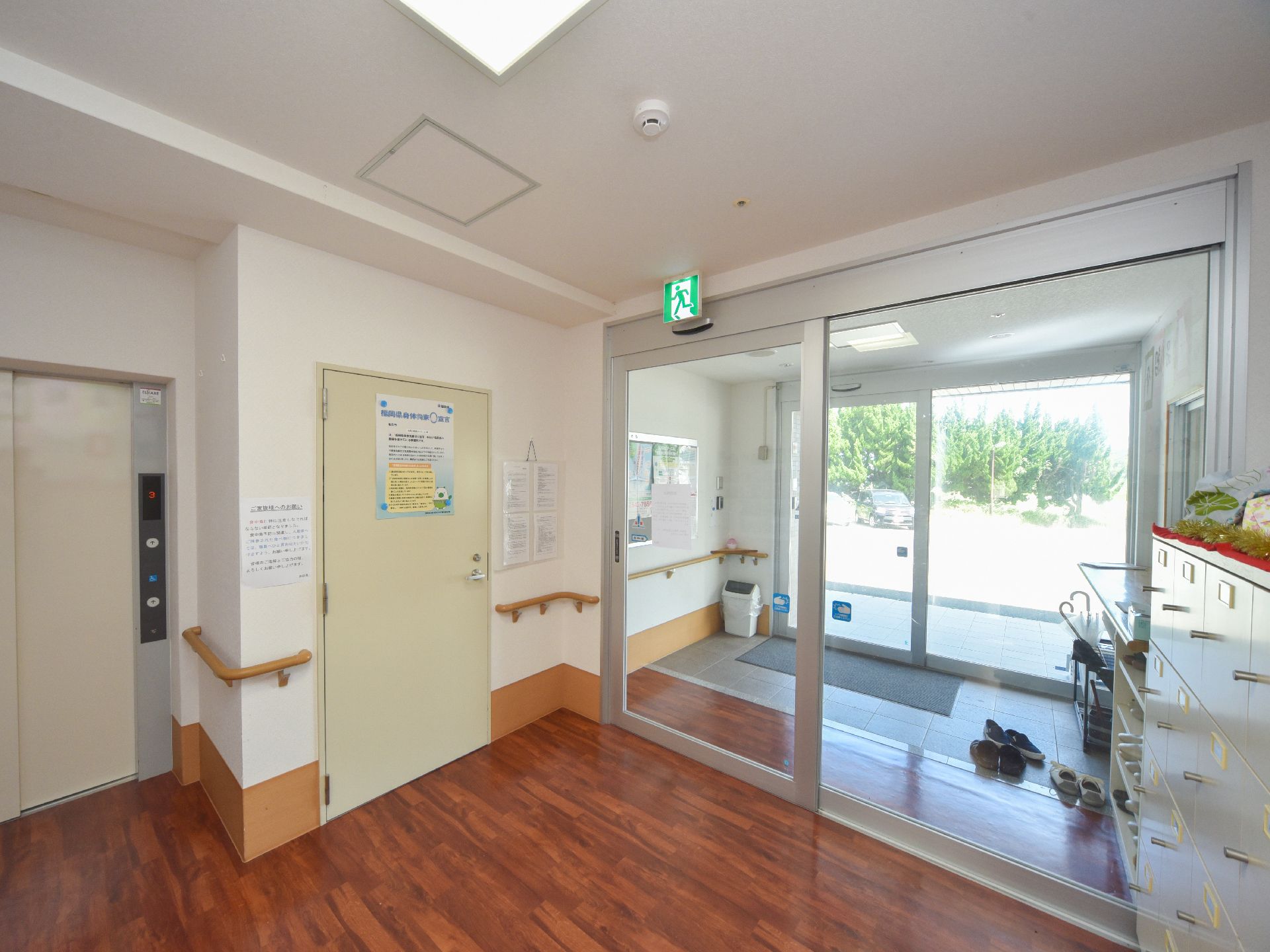 外部の空気を取り込まないように風除室になっており壁に掲示板があり、連絡事項などが掲示されている。木製の手摺が設置されている。