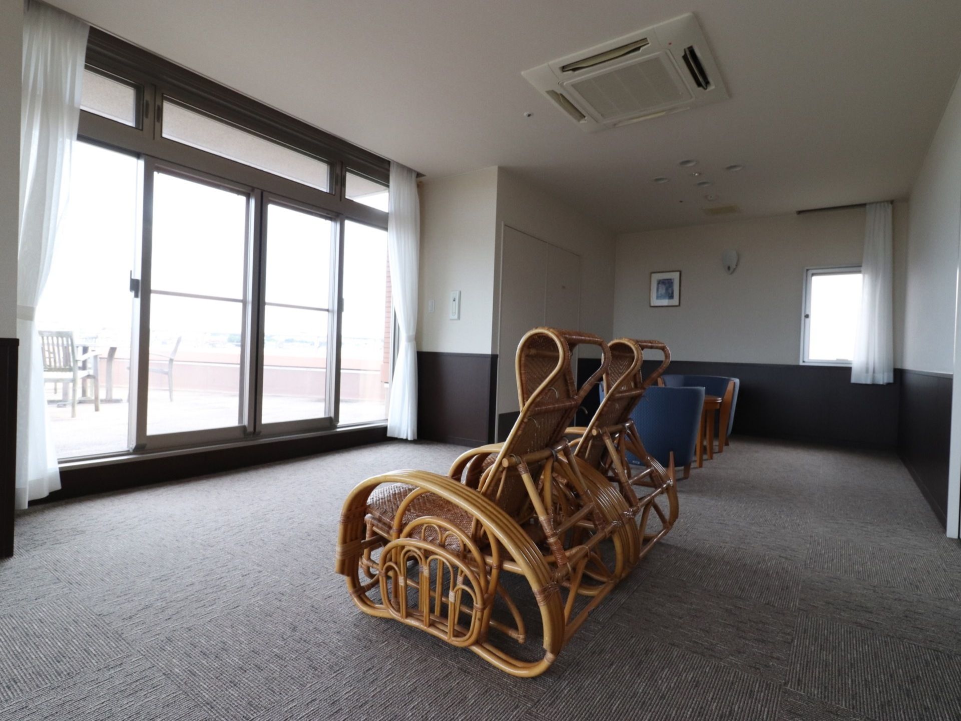 大きな窓のある部屋に、2種類の椅子が2脚ずつ置かれている。床は絨毯が敷かれ、窓の外にはテーブルと椅子が見える。