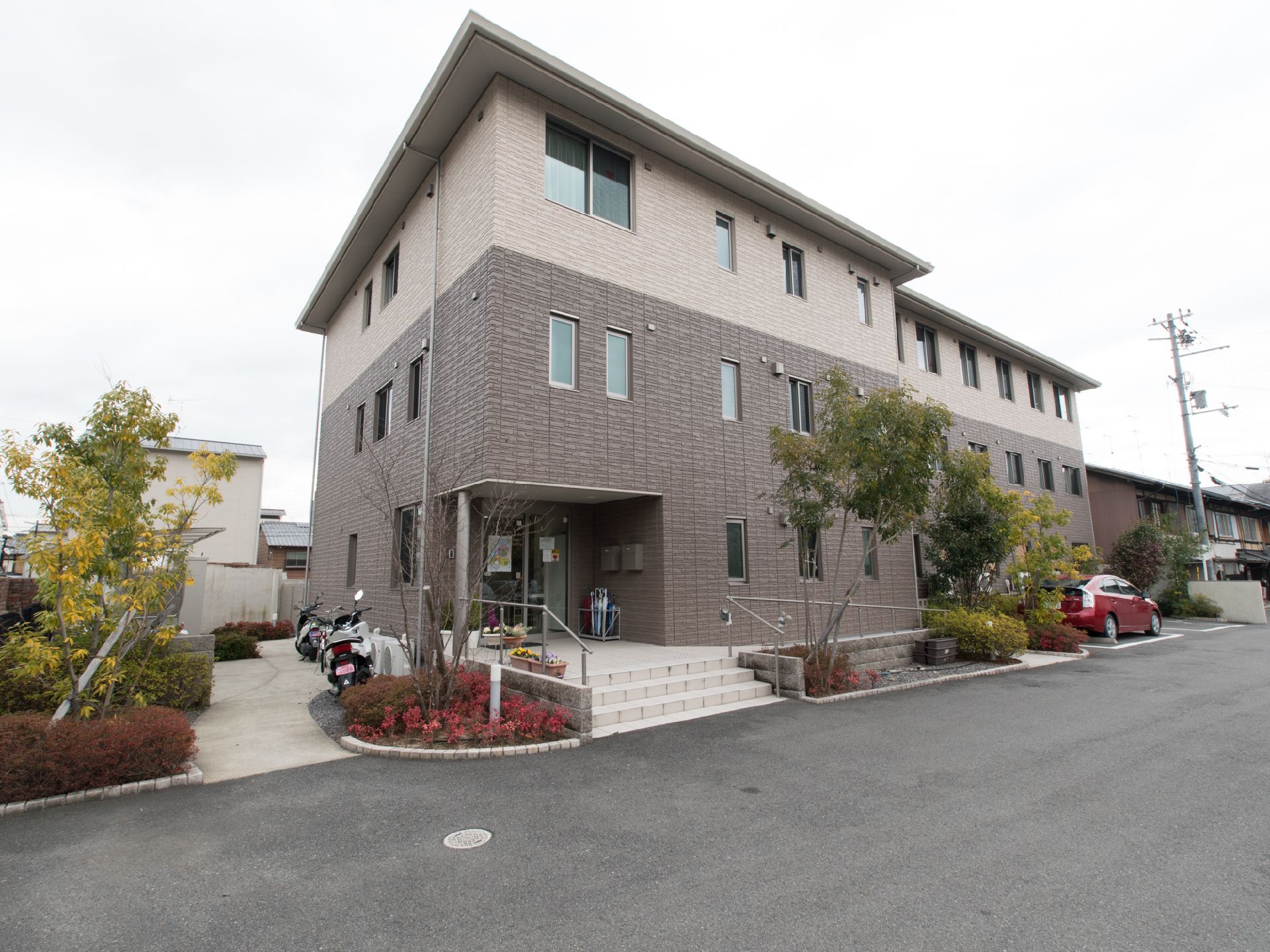 建物は3階建て。階段とスロープが設置されている。建物の周囲には、手入れをされた植物が植えられている。