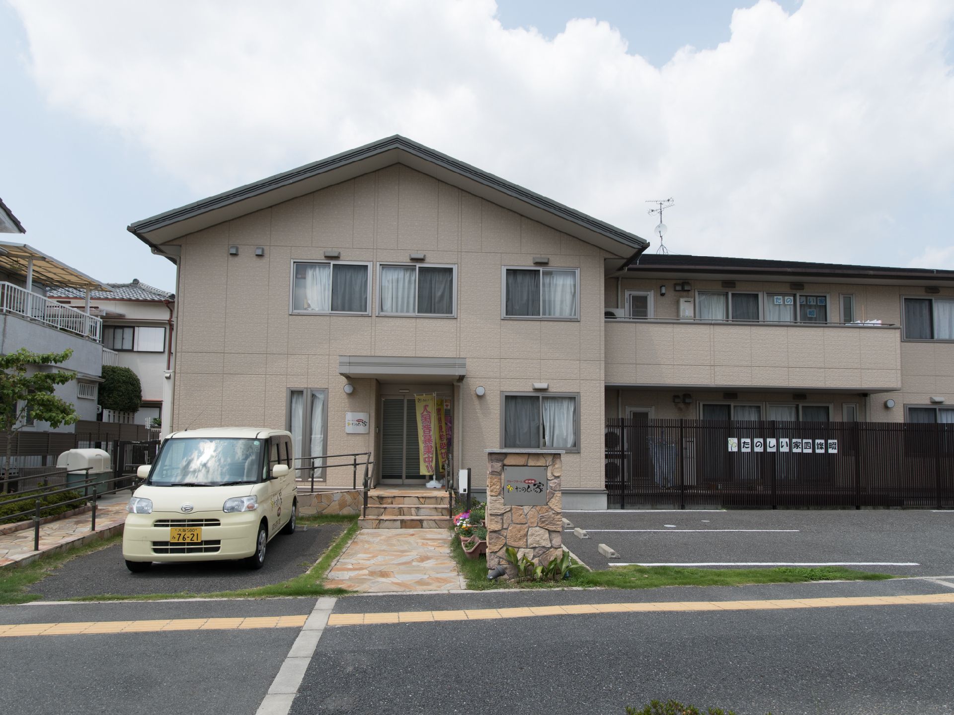 建物は2階立て。建物の前に駐車場がある。階段とスロープが設置されている。手摺もある。建物の脇にゴミ収集場がある。