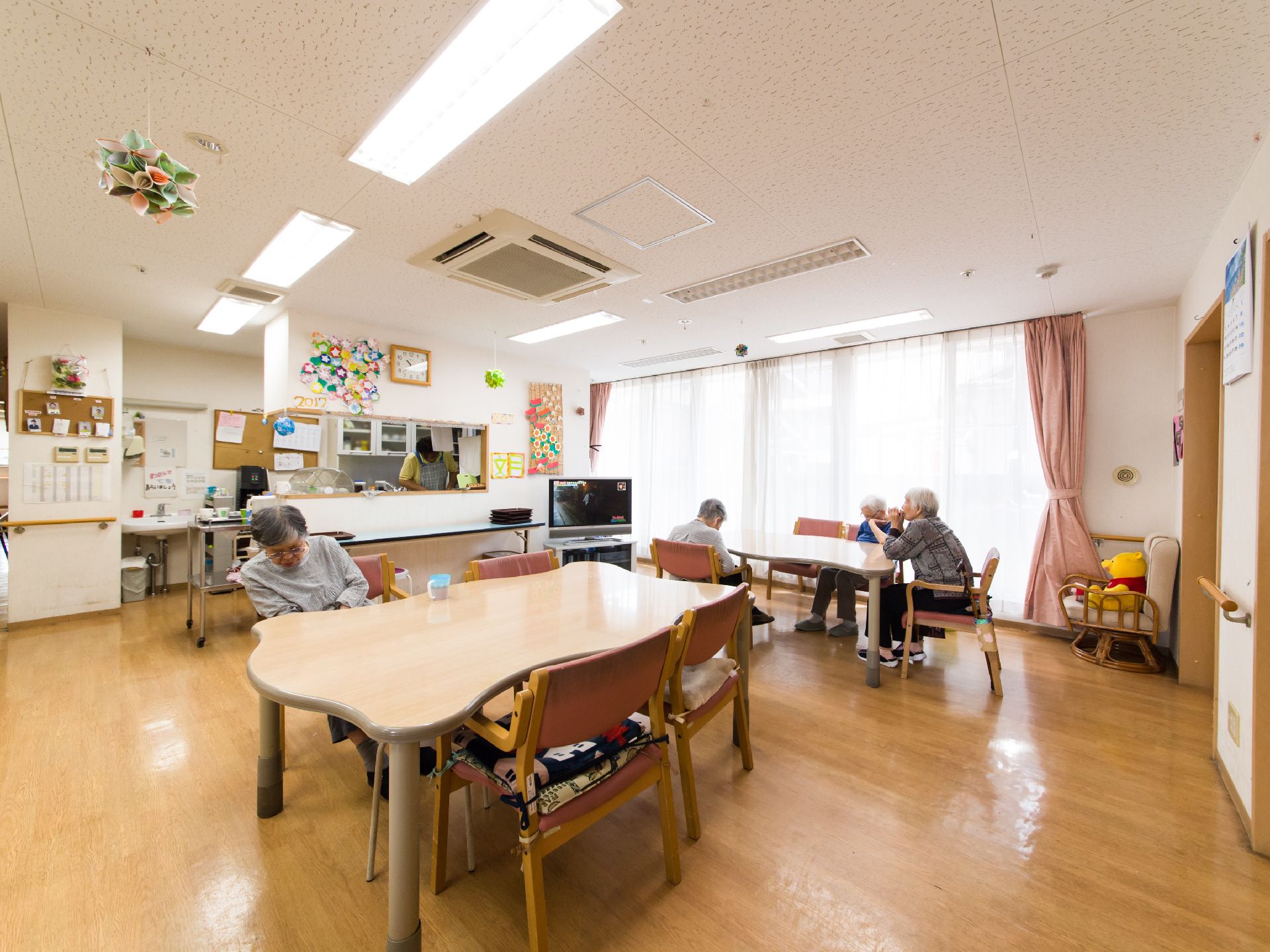 手作りのガーランドが天井からかざってある食堂で、入居者が四名椅子に座っているのが見える。キッチンでは、スタッフが作業をしている。