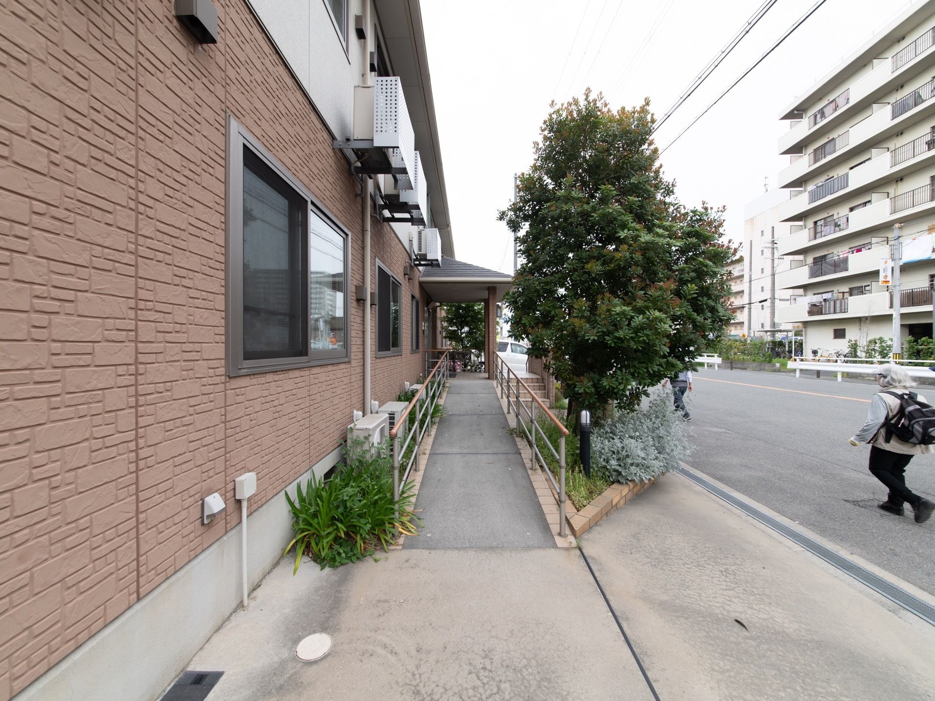 玄関への入口は歩道から緩い傾斜のスロープが繋がっている。スロープ沿いにはさまざま樹木が植えられている。