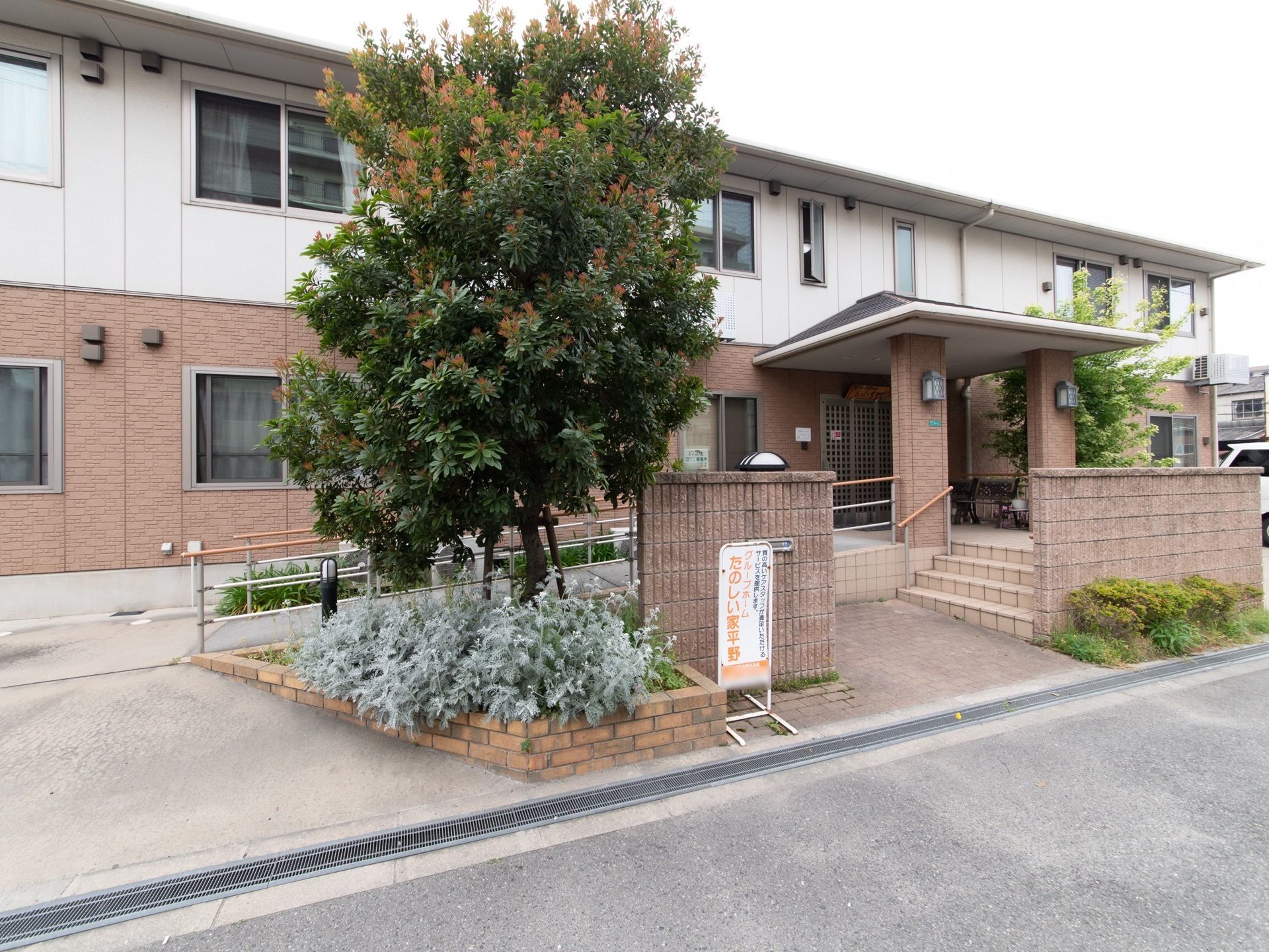 ２階建ての建物は、１階がピンク、２階が白に塗り分けられている。玄関はスロープと階段が用意されており、入口周りは植物が植えられている。