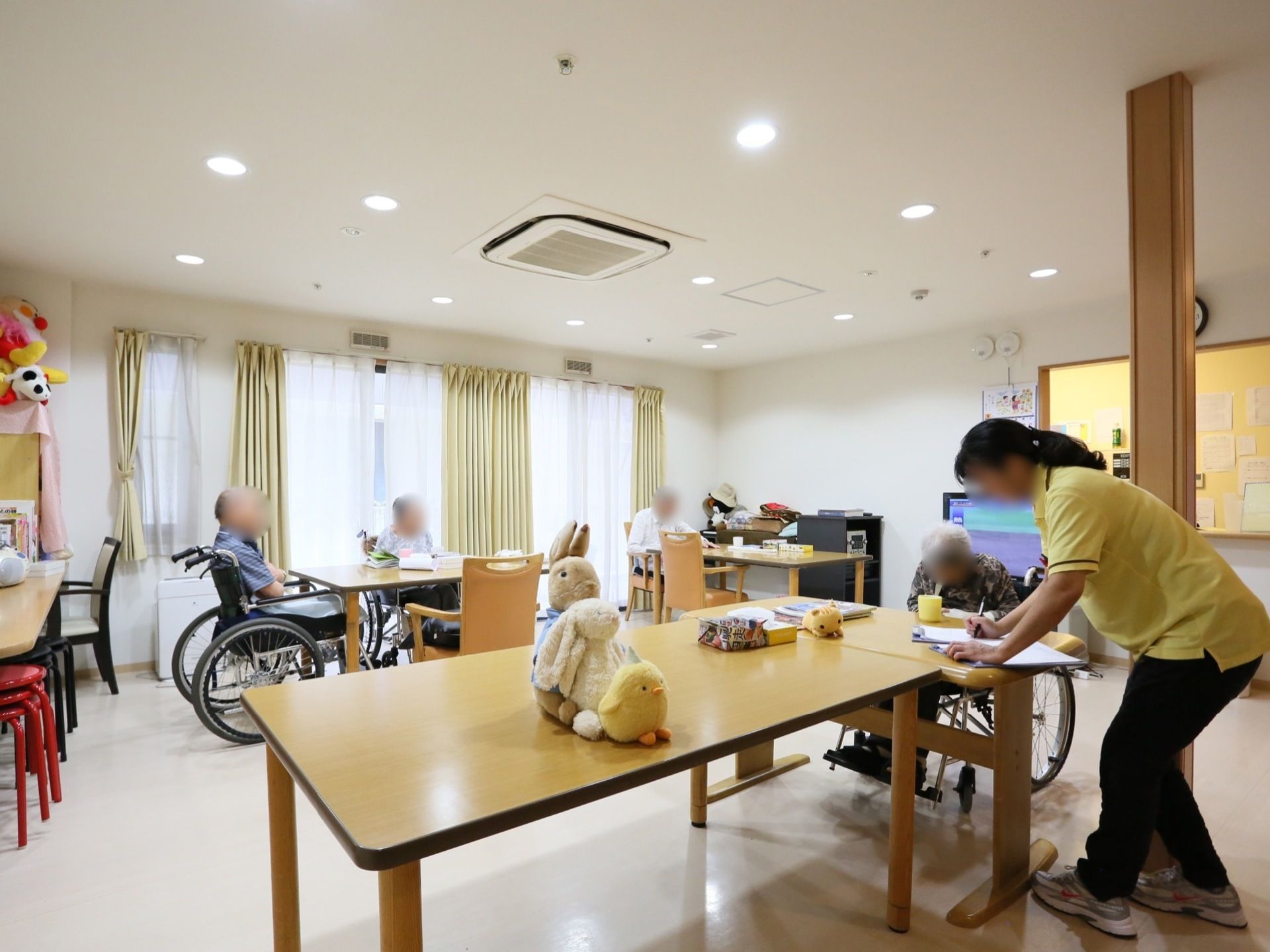 広々としたスペースで、テーブルや棚の上にさまざまなぬいぐるみが置かれている。複数の入居者様が過ごされている。