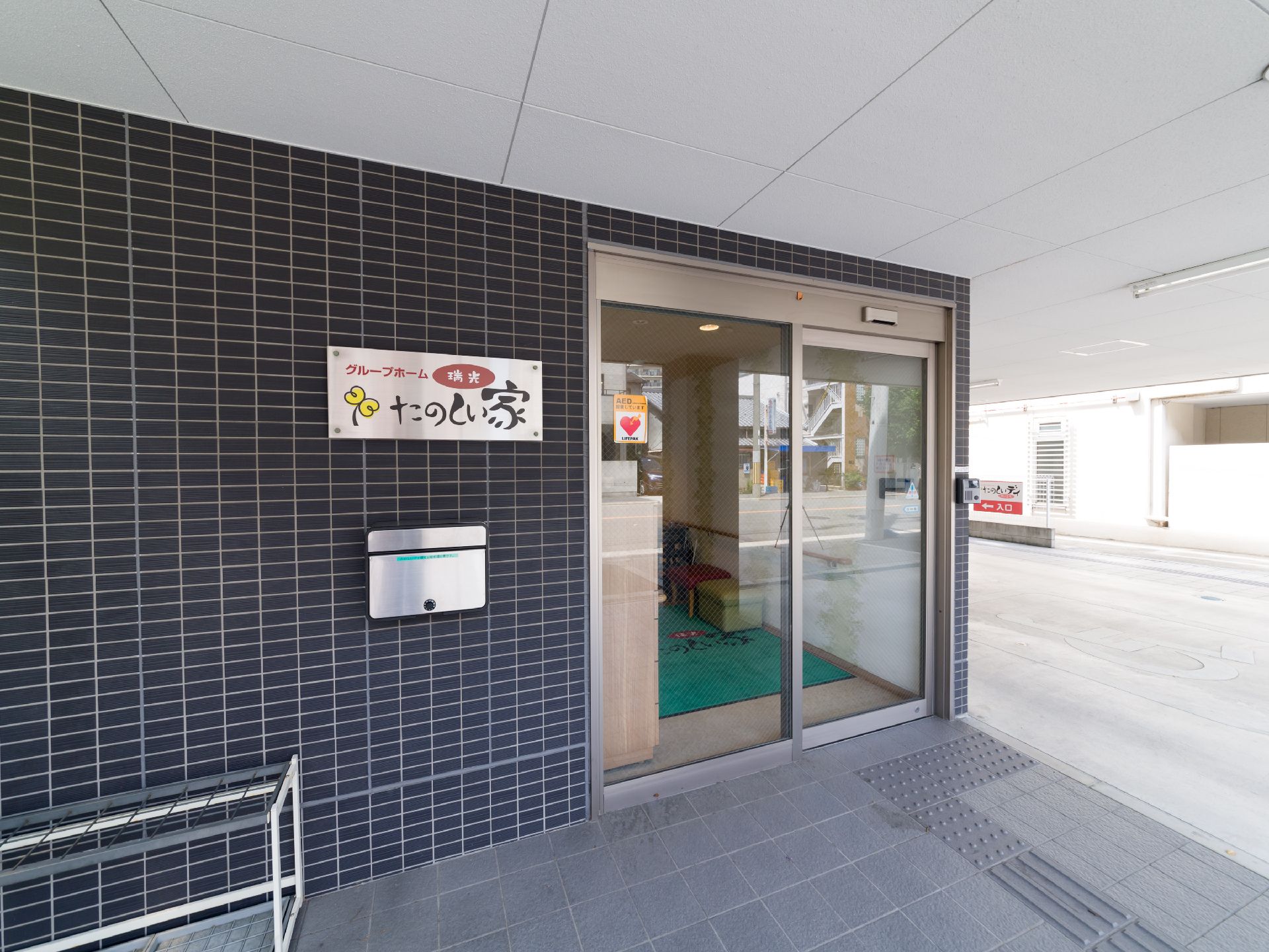 壁や床がタイル張りで、自動扉の左横に看板が掲げられている施設玄関