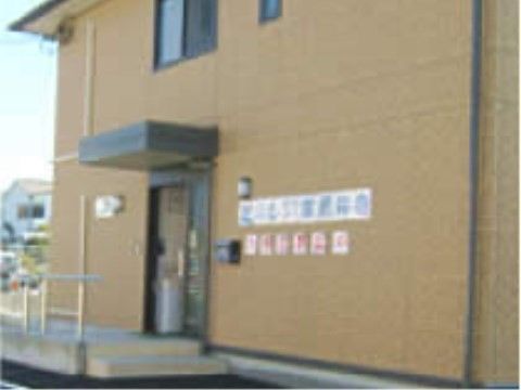濃いベージュ色の外壁の2階建ての建物である。1階のひさしのある玄関の横に、横書きで施設名称を表示している。