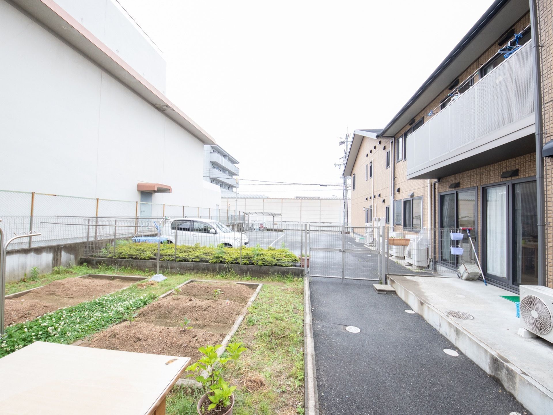 施設のリビングの窓から見える位置に花壇が整備されている。その奥のフェンスの向こう側には駐車場が見える。