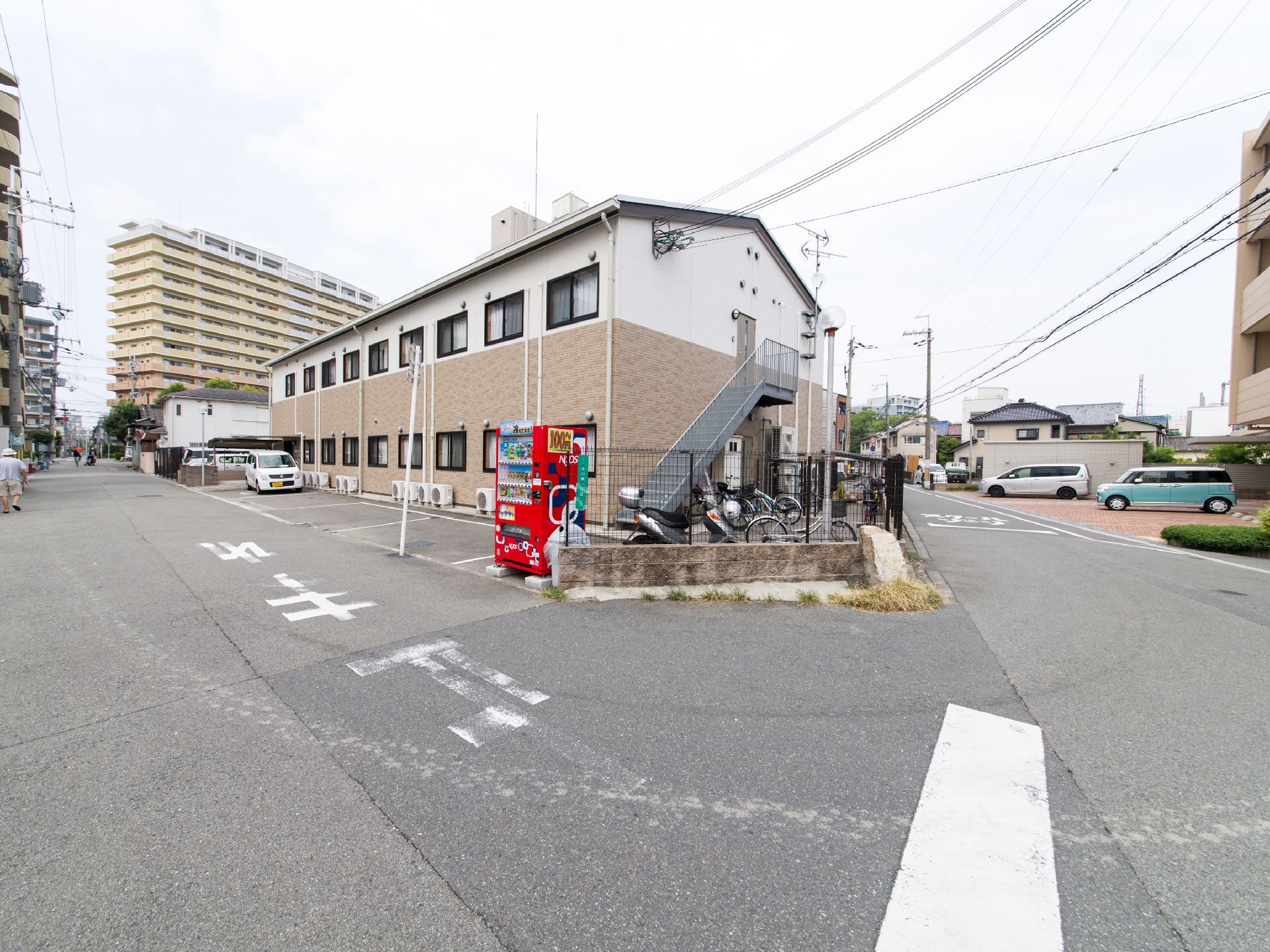 二階建ての施設は、一階部分が茶色、二階部分の外壁が白である。外から二階へ行くことができる階段がついている。スクーターが一台とまっている。
