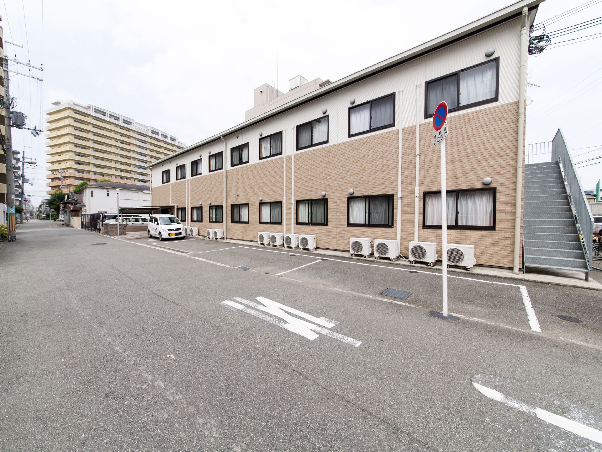 施設は、二階建ての建物で、敷地内に駐車場が設けてある。車が一台とまっている。駐車場そばに自動販売機がおいてある。
