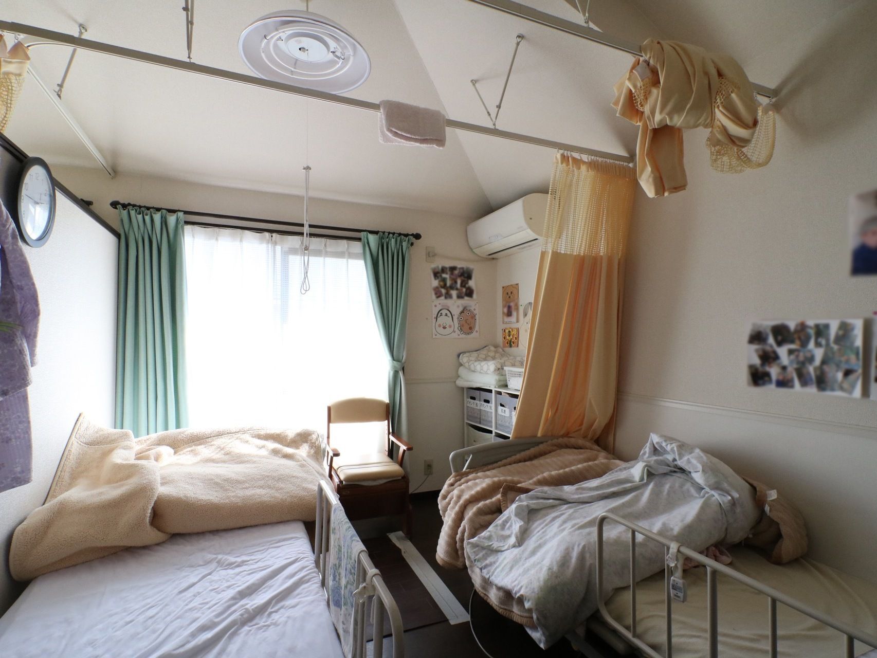 柵のついたベッドが２台置いてある。天井から間仕切り用のカーテンが吊るされている。壁には時計やエアコン写真が飾られている。