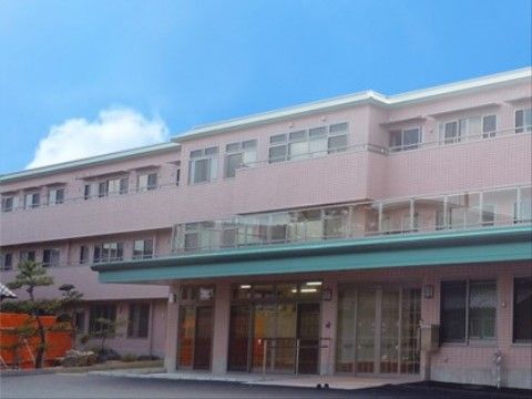 玄関前に緑色の屋根がせり出した、３階建てのピンクの施設