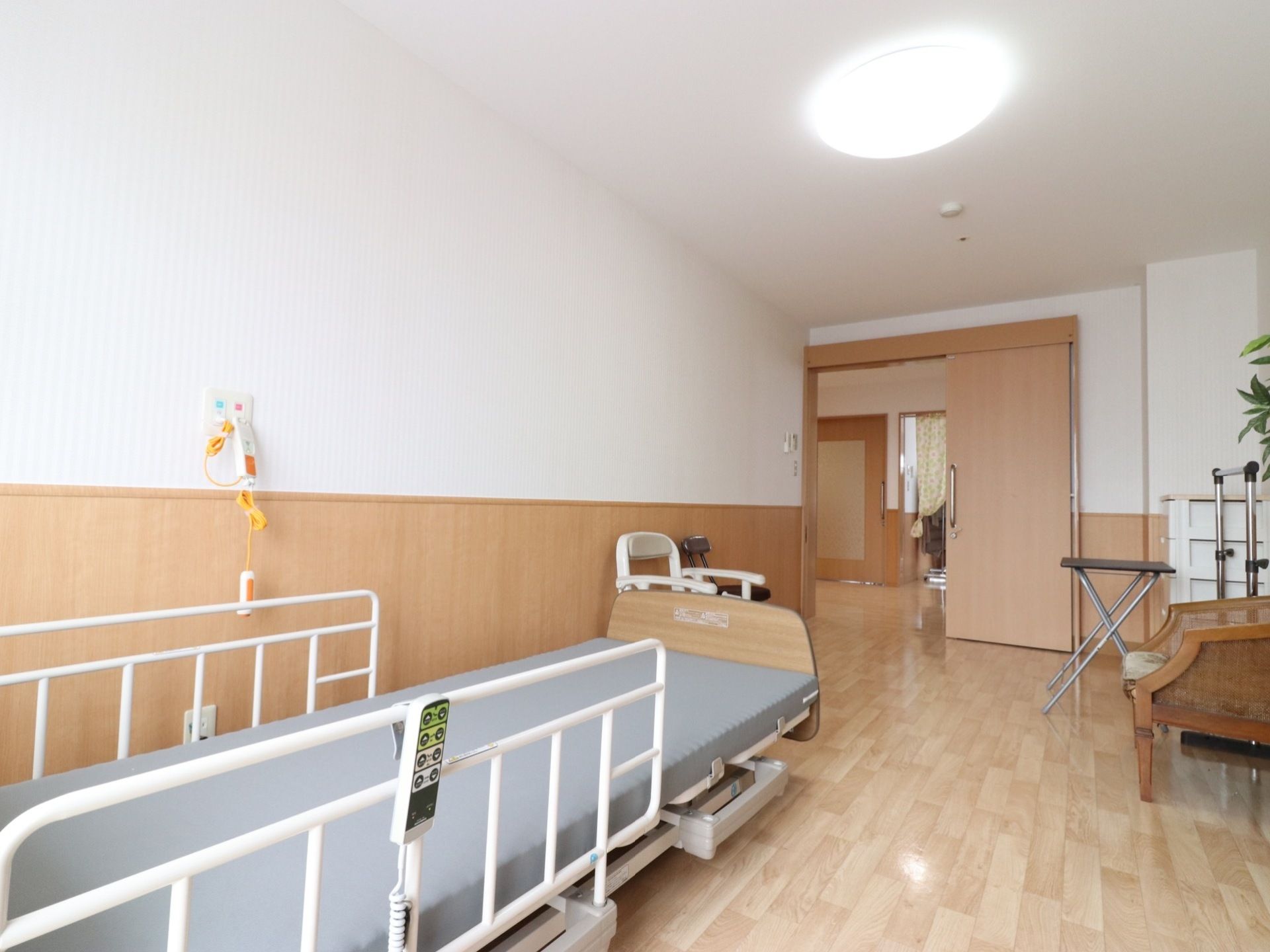 居室の床はフローリングで、入り口の扉は木製の引き戸である。左の壁際にフェンス付きの電動ベッドを設置している。