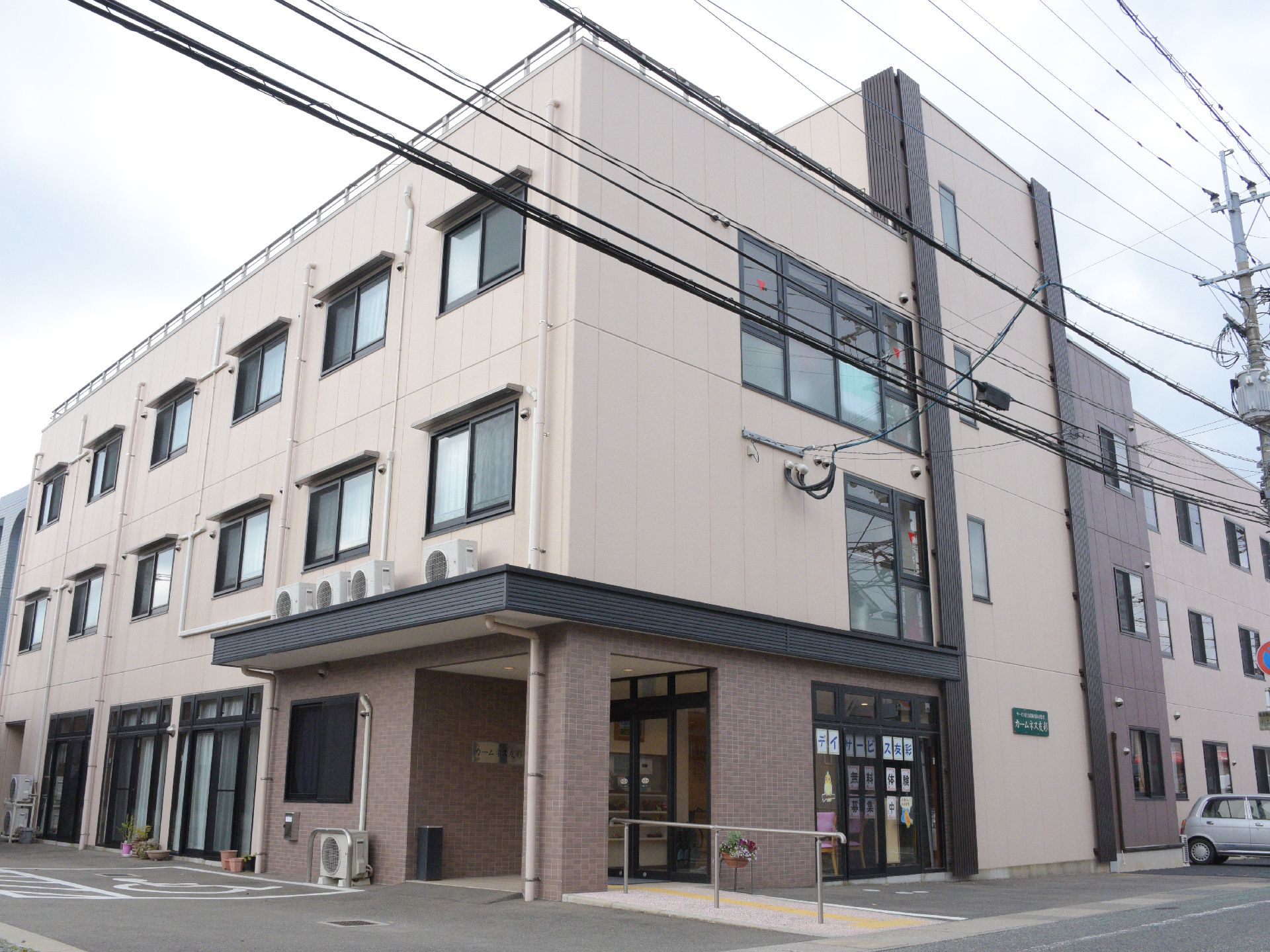 交差点の角地に建つ、薄いピンク色に塗られた３階建ての建物
