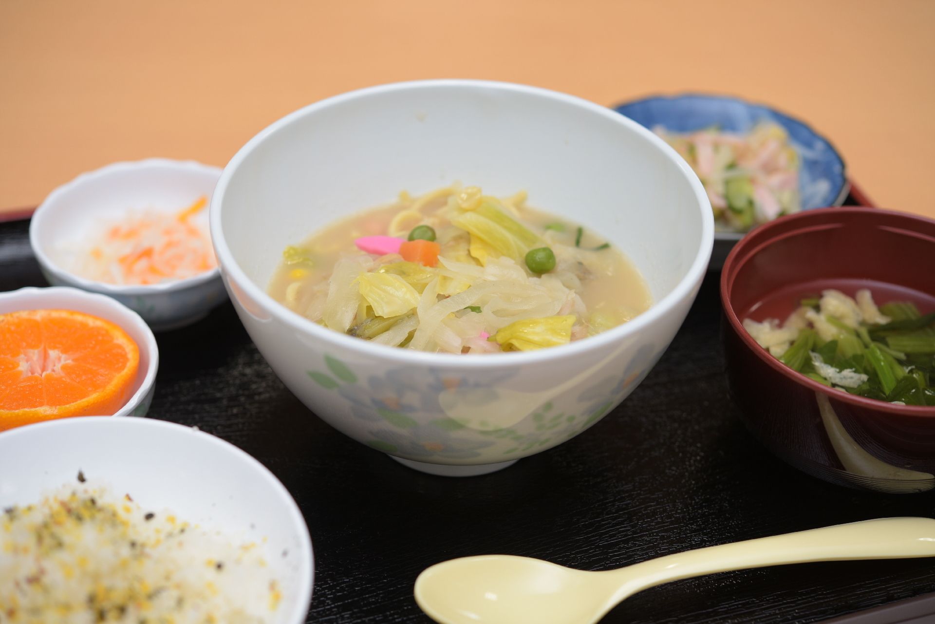 ちゃんぽん麺、スープ、ごはん、副菜2つ、デザートのみかんがトレイに並べられている。入居者様の栄養バランスにも気が使われている。