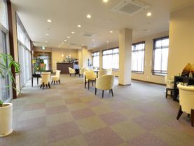 ラウンジの両側には大きな窓があり明るい光が差し込んでいる。茶色のテーブルと白いイスが並んでいる。観葉植物なども置いてある。