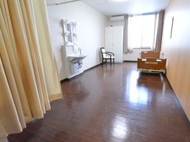 白い壁と木目調の床が落ち着いた雰囲気の居室である。白い家具やライトブラウンのベッドが置かれている。エアコンも付いている。