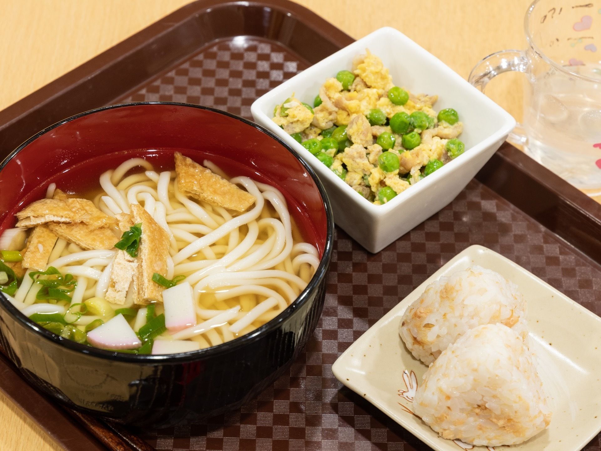 食事は一人ずつ黒いお盆の上に配膳される。きつねうどんと小さなおにぎり２つ、グリーンピースの卵とじのメニューである。