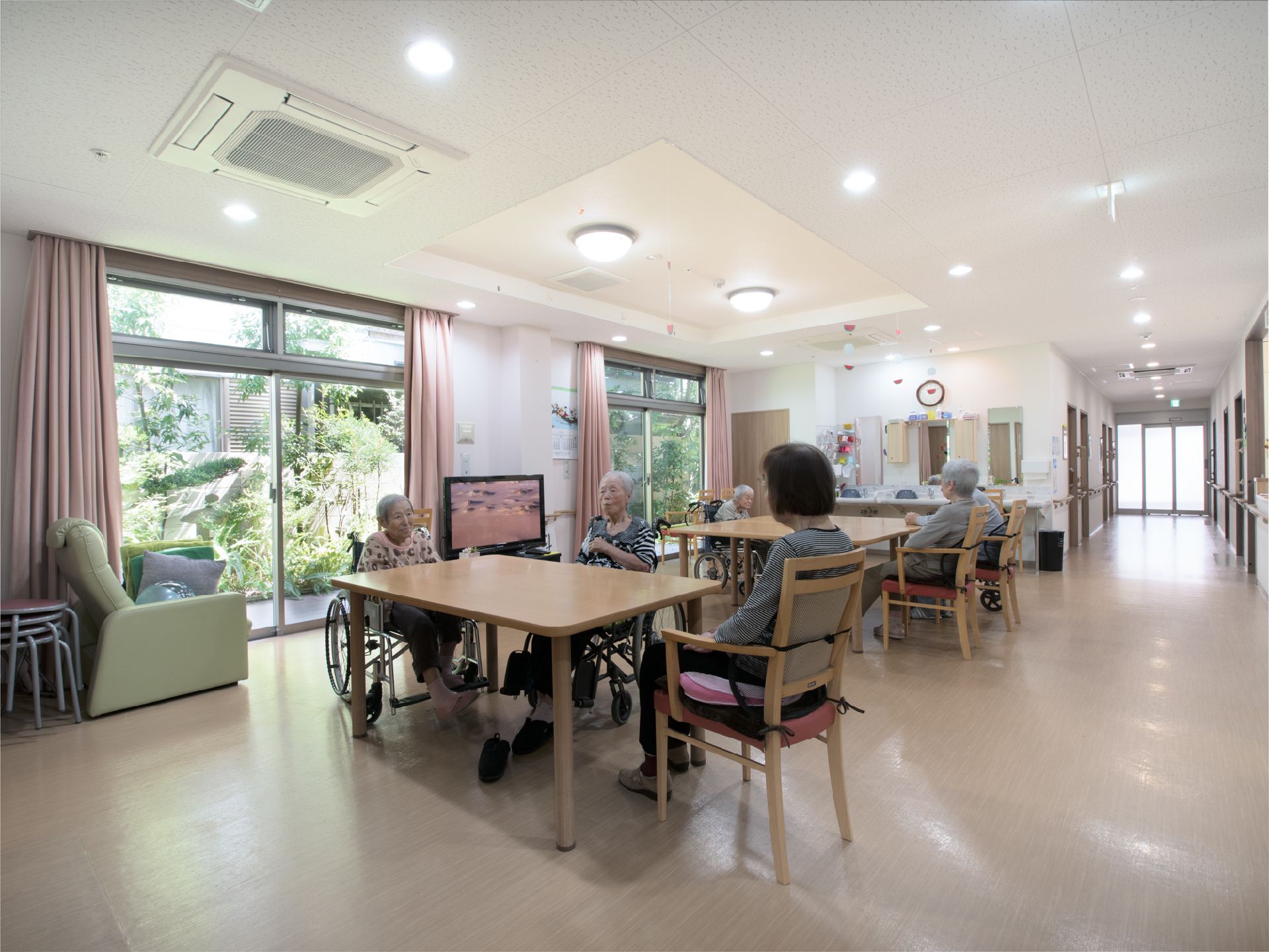 掃き出し窓があり、そこから庭がみえる食堂には、机が二台あり、六名の方が利用をしている。テレビがついている。