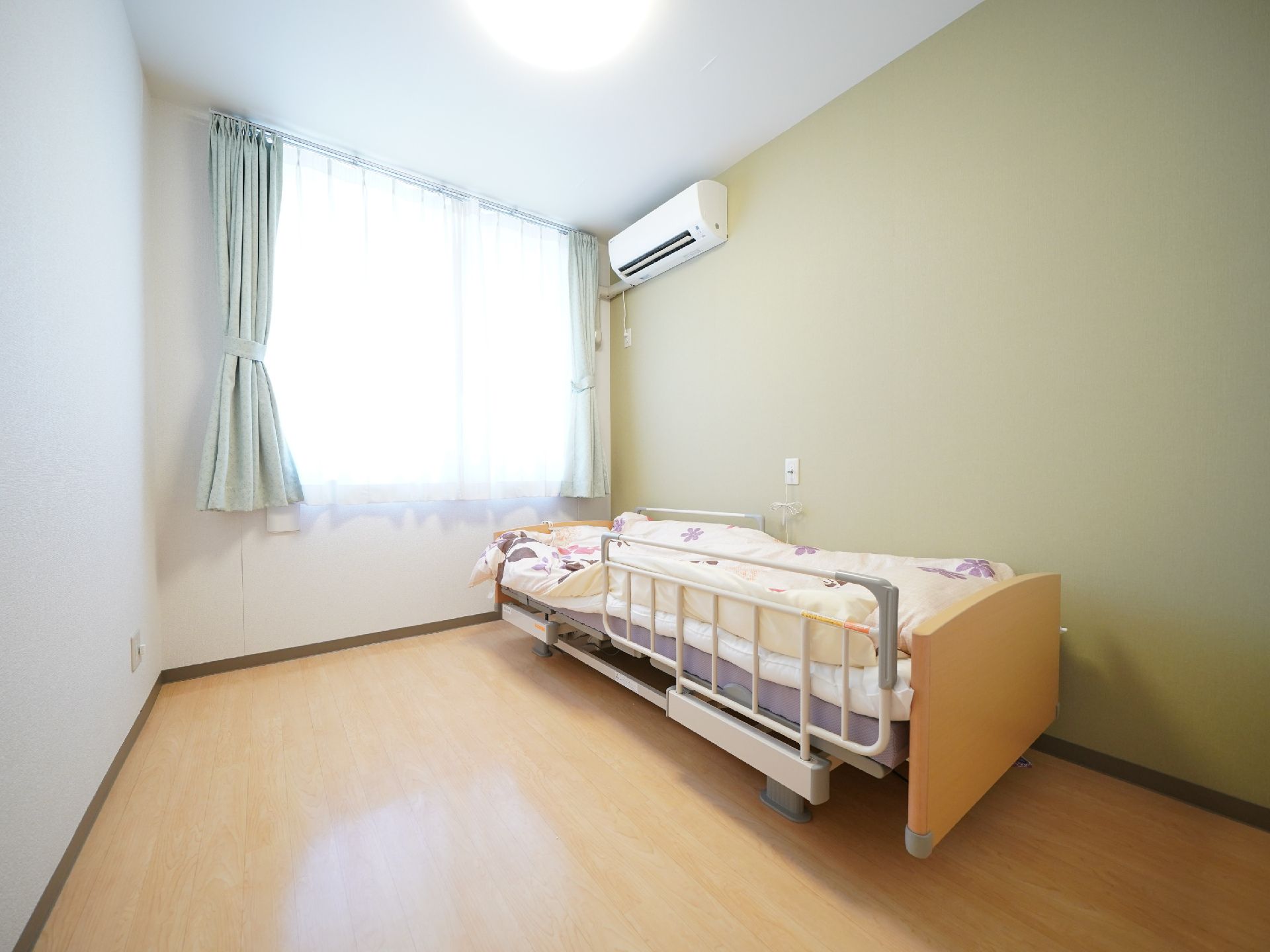 花柄の布団が敷かれたベッドやエアコン、カーテンが付いている部屋