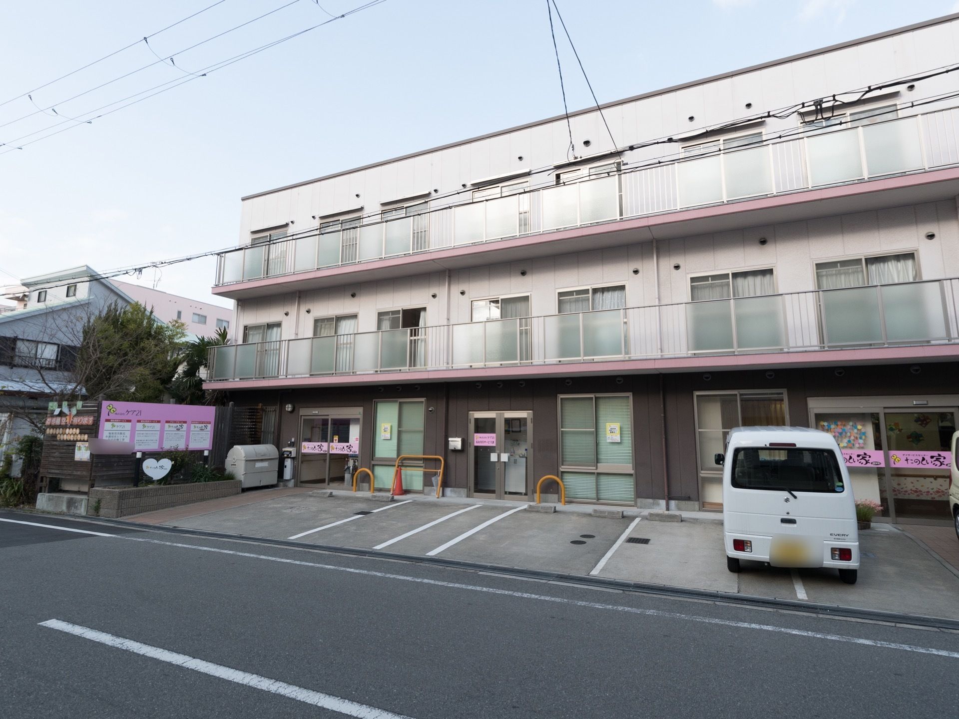 施設は白色とピンク色を基調とした外観である。入口のすぐ側には複数の車が停めておけるようになっている。