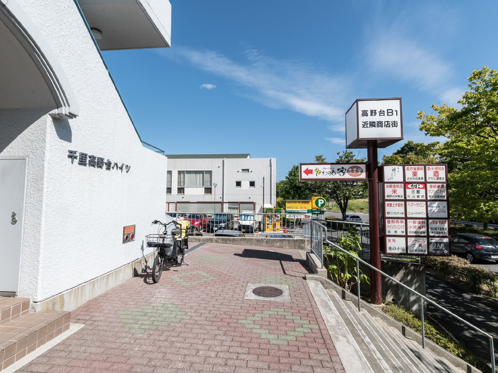 画像左側には施設の入り口がある。また、その近くの壁際に1台の自転車が止められている。奥には駐車場もみえる。