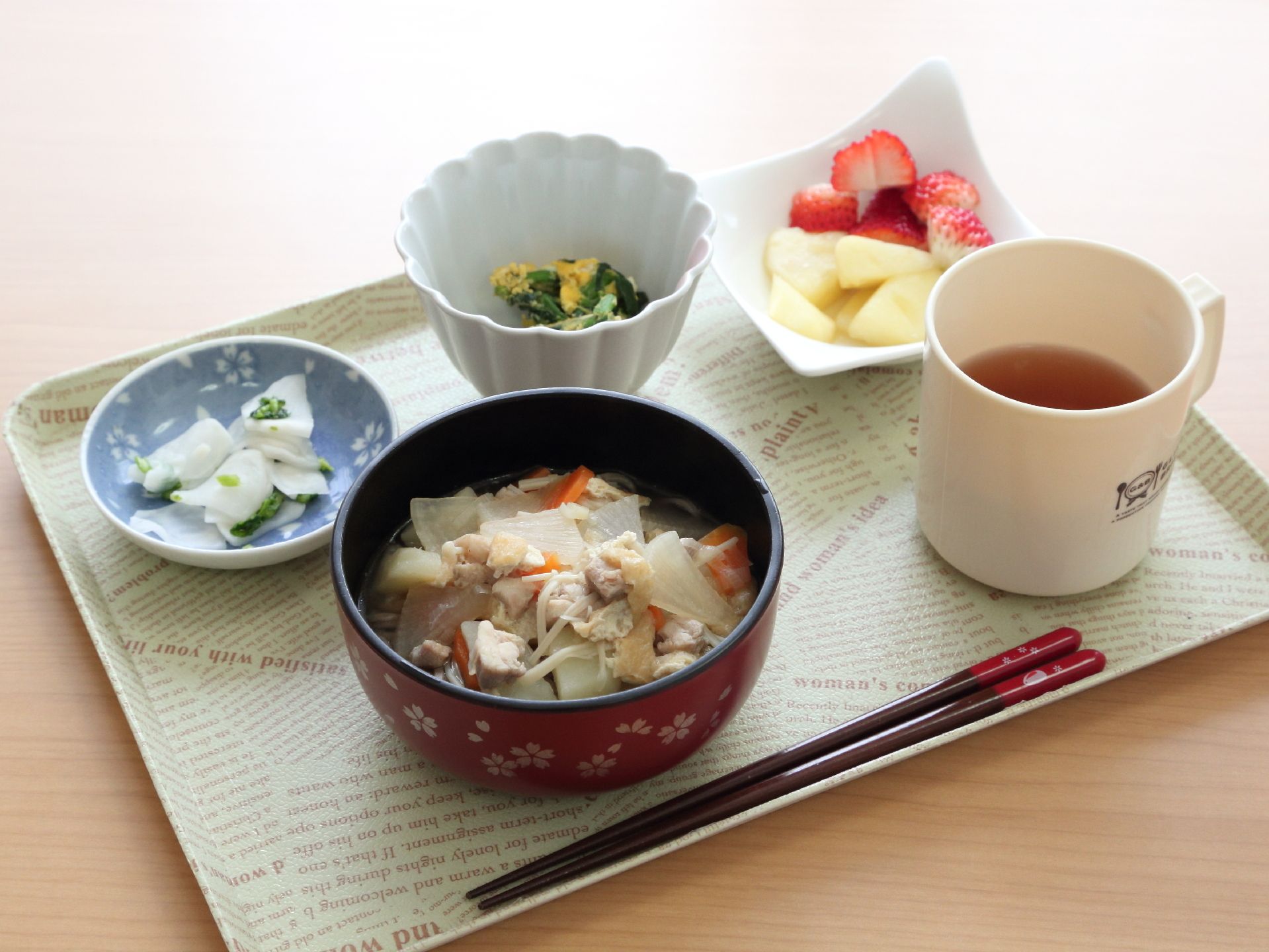 ある日の食事メニュー。主菜と主食が一緒になったけんちんうどん、副菜2種に果物がついている。お茶も含め1つのトレーに乗せられている。
