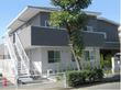 1階が白、2階がグレーの外観で2階建てになっている。側面には非常階段があり、建物前に大きな木が植わっている。