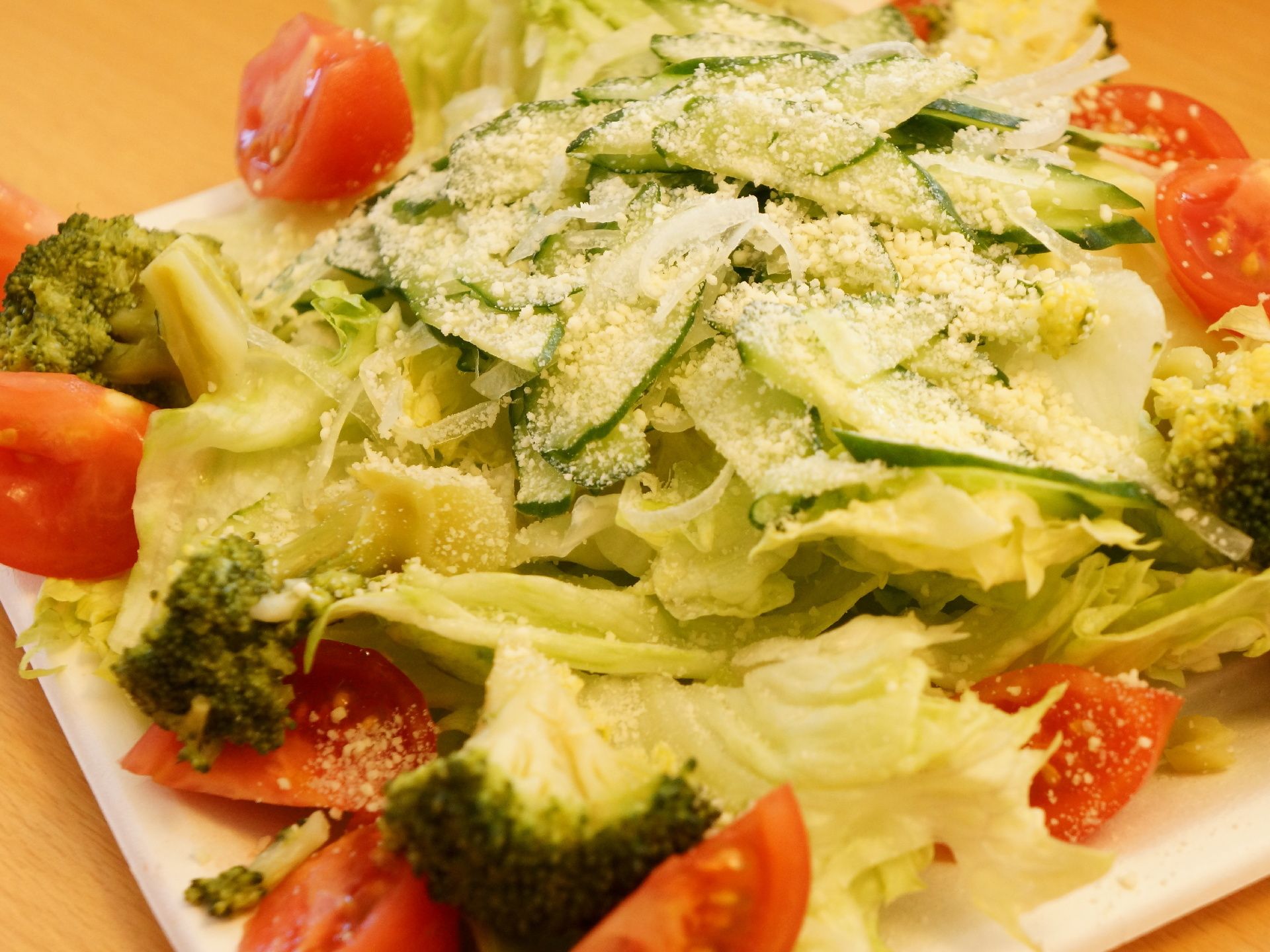 新鮮野菜のトマト、キャベツ、ブロッコリー、キュウリの盛り合わせで、粉チーズが掛けられ、イタリア風である。