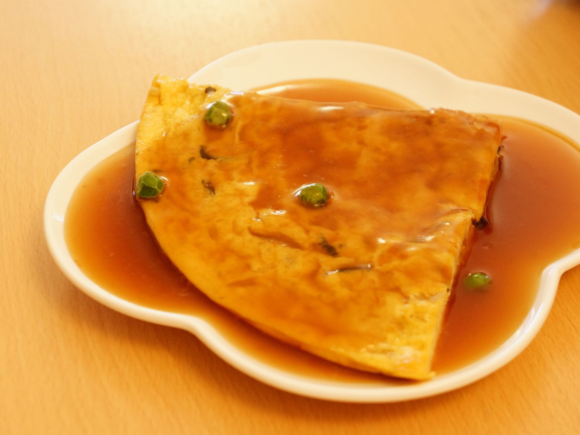 かに玉あんかけにグリンピースが散りばめてある。器は、四つ葉風で浅めのデザインである。大きなかに玉を4等分して提供している。