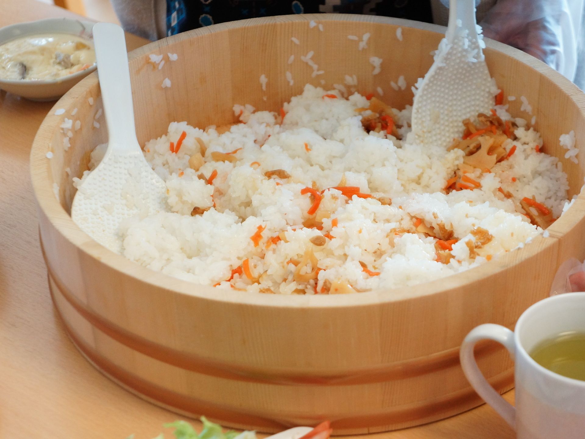 五目ずしを作っている。レンコン、ニンジンなど根菜を別に煮つけ、酢飯と混ぜている。これを混ぜる時は二人で行う。