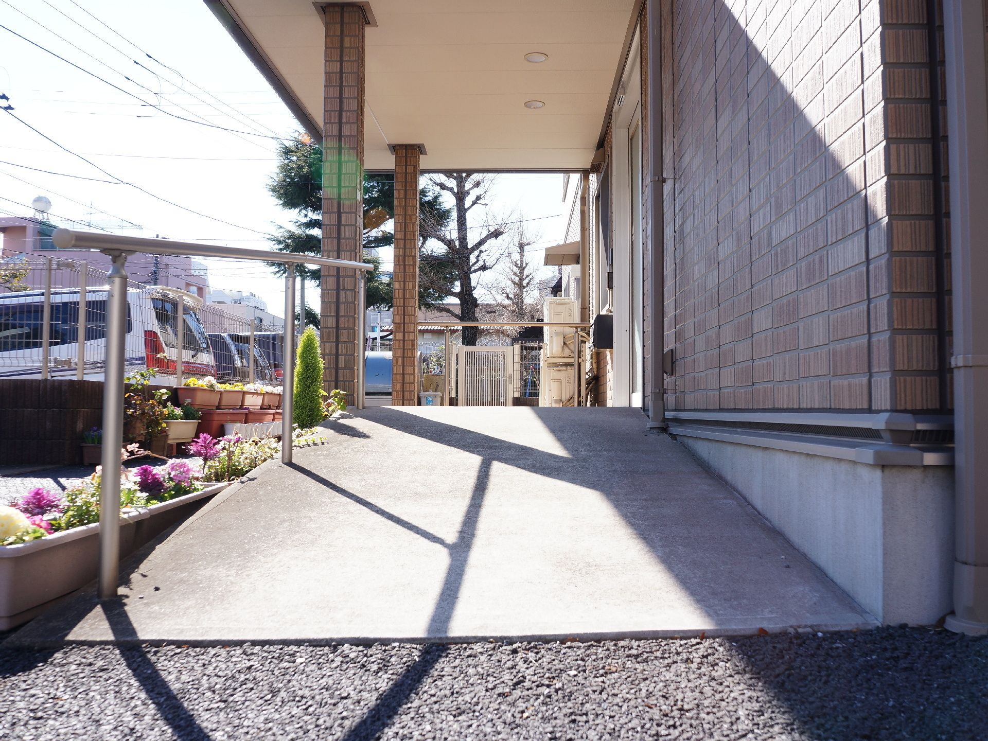 玄関のスロープに手すりが取り付けられている。スロープ横には花が植えられている。玄関横にポストとインターホンが取り付けられている。
