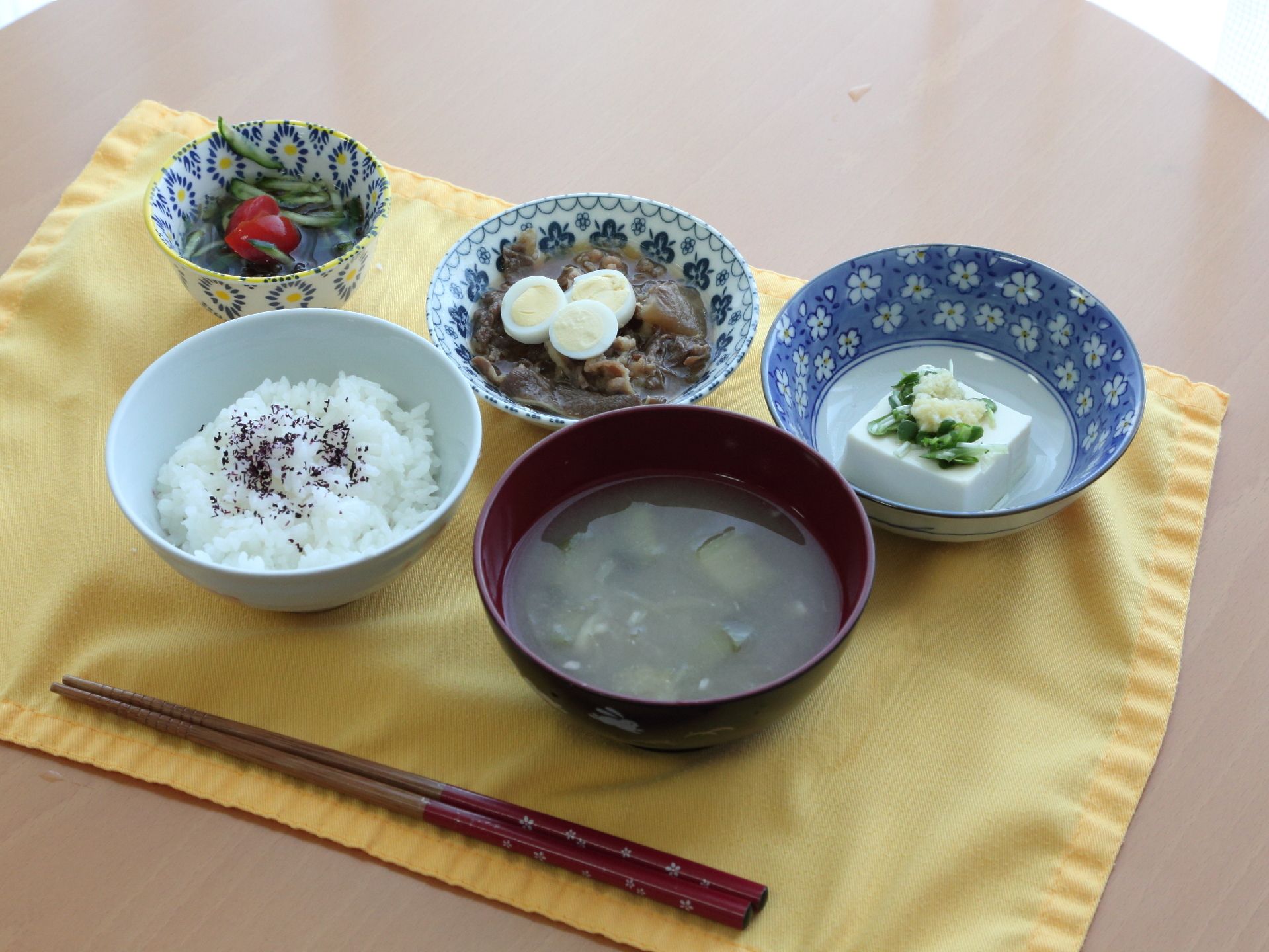 黄色いランチョンマットに並べられた、牛肉の煮物などの食事