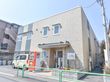 施設の外観の写真である。建物は2階建てで、入り口には看板が立っている。看板の隣には自動販売機が設置されている。