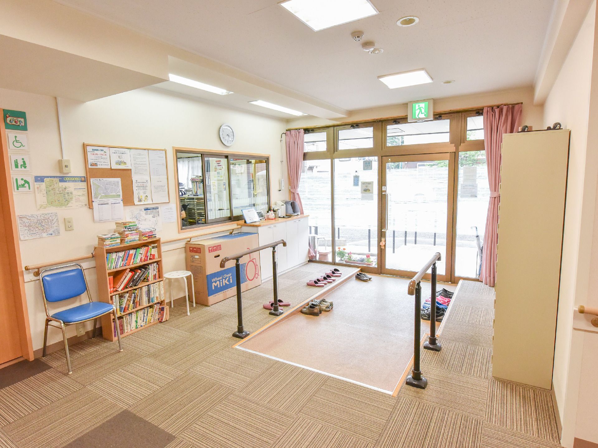 施設玄関は手すり付きのスロープになっていて、靴が並んでいる。大きさの違う椅子の真ん中には本棚が置かれている。