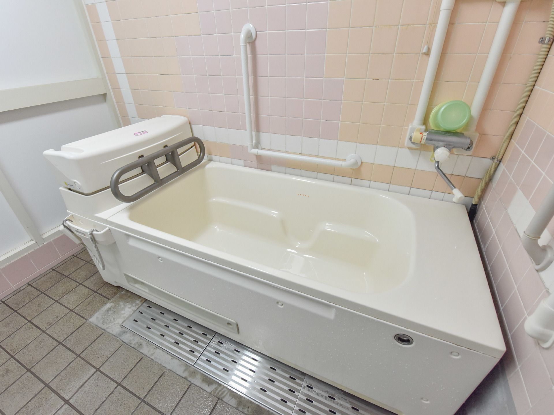 介助を受けて入浴ができる介護用の浴槽がある。ピンクのタイルの壁には手すりがついていて、安全に入浴ができる。