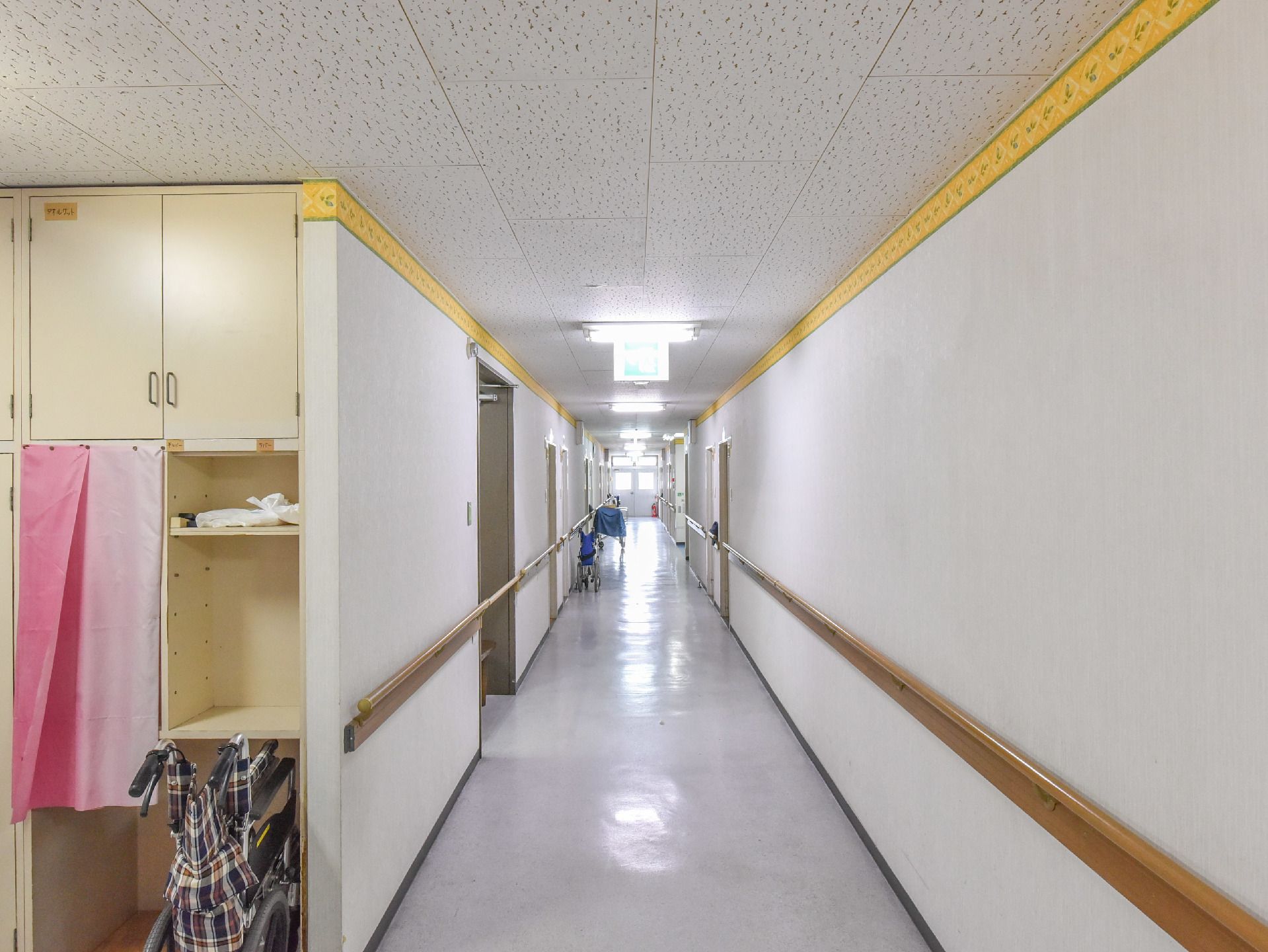 白壁に木目の手すりが取り付けられている。幅にゆとりがある廊下で、車いすの方もゆったり移動することができる。
