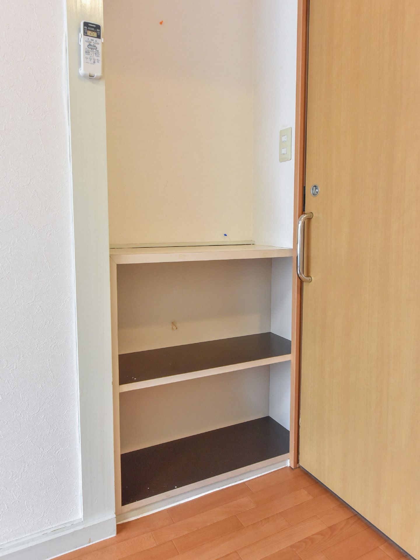 入口を入ってすぐのスペースに棚がある。2段あり色々な使い方ができる。エアコンがあり、リモコンが棚近くの壁に設置されている。
