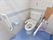 タイルの壁に水色の床のトイレは、手すりが便器の脇と前についていて安心して利用できる。温水洗浄便座で便利になっている。