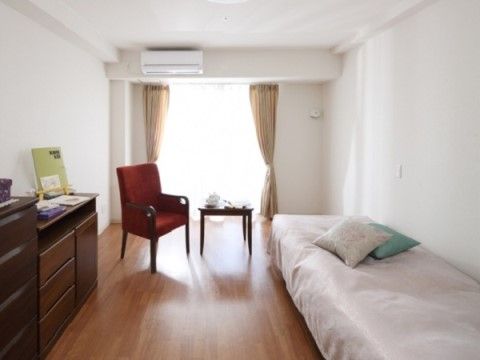 壁紙に白色が使われており、室内が明るく感じられる。ベッドから近くには椅子やテーブルがあり、タンスなどの家具が置かれている。